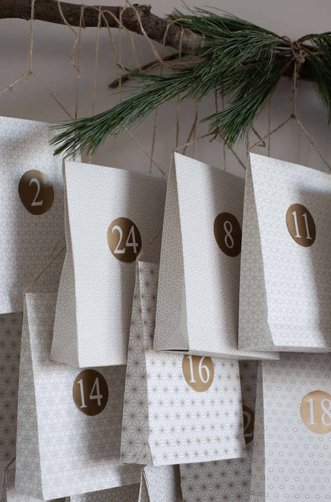 Calendrier de l'avent avec de beaux petits paquets cadeaux très classes blancs et dorés suspendus à une branche de sapin_l'atelier en ville _nivelles