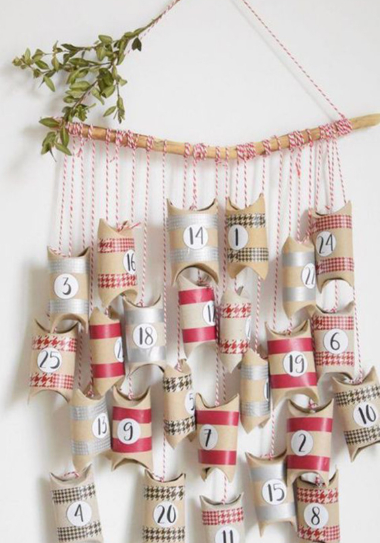 Calendrier de l'avent avec plein de petites boites cadeaux décorées aux couleurs de noël suspendues à un bois flotté