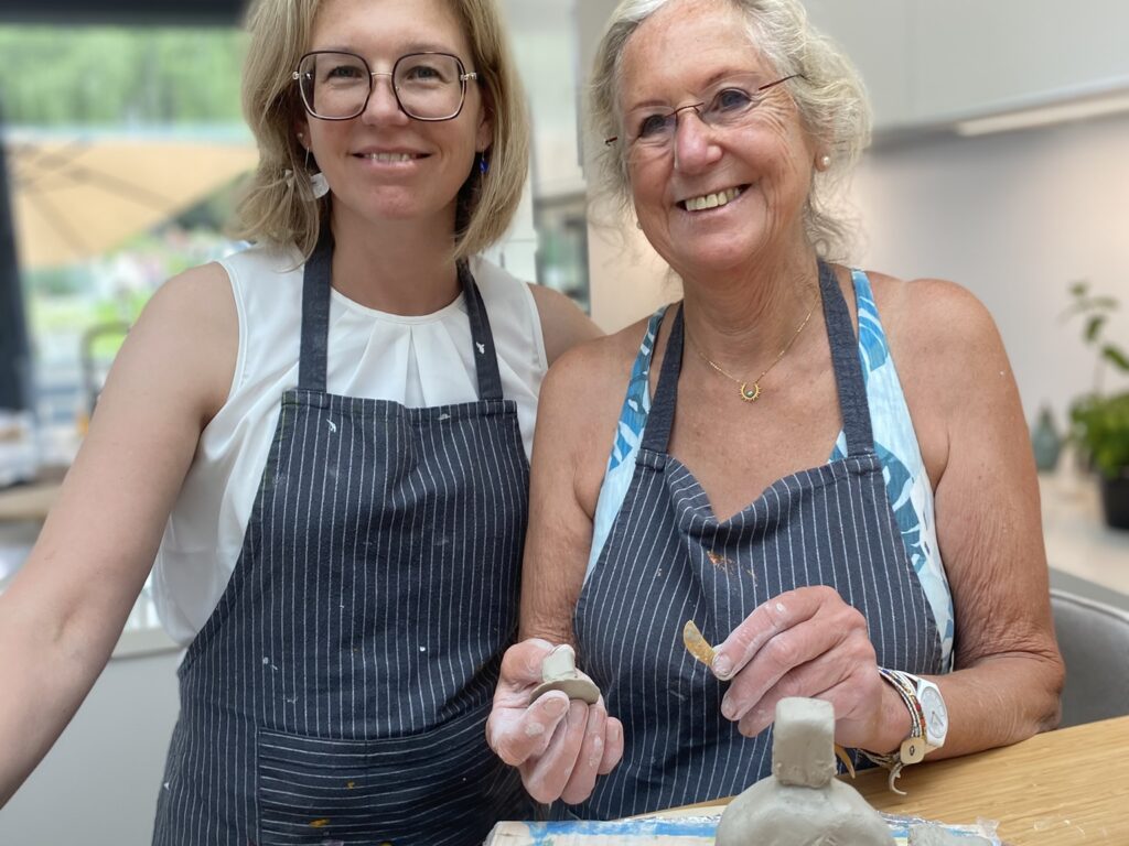 Deux femmes souriantes en tablier créant des sculptures en argile à L'Atelier en Ville à Nivelles
