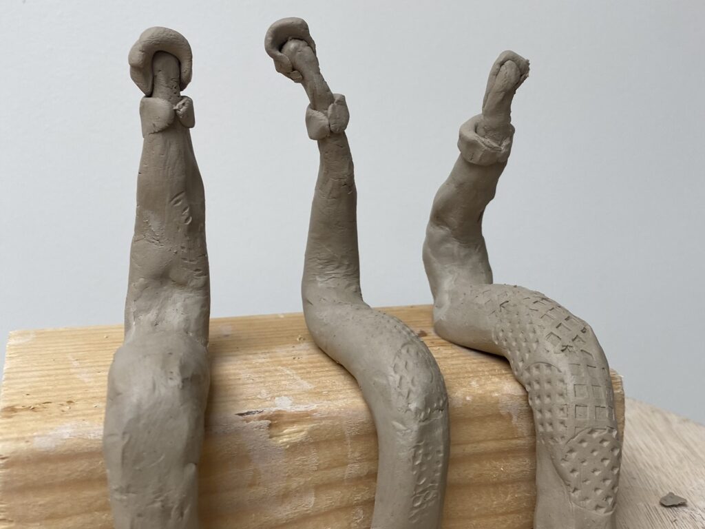 Trois sculptures abstraites en argile alignées sur un support en bois